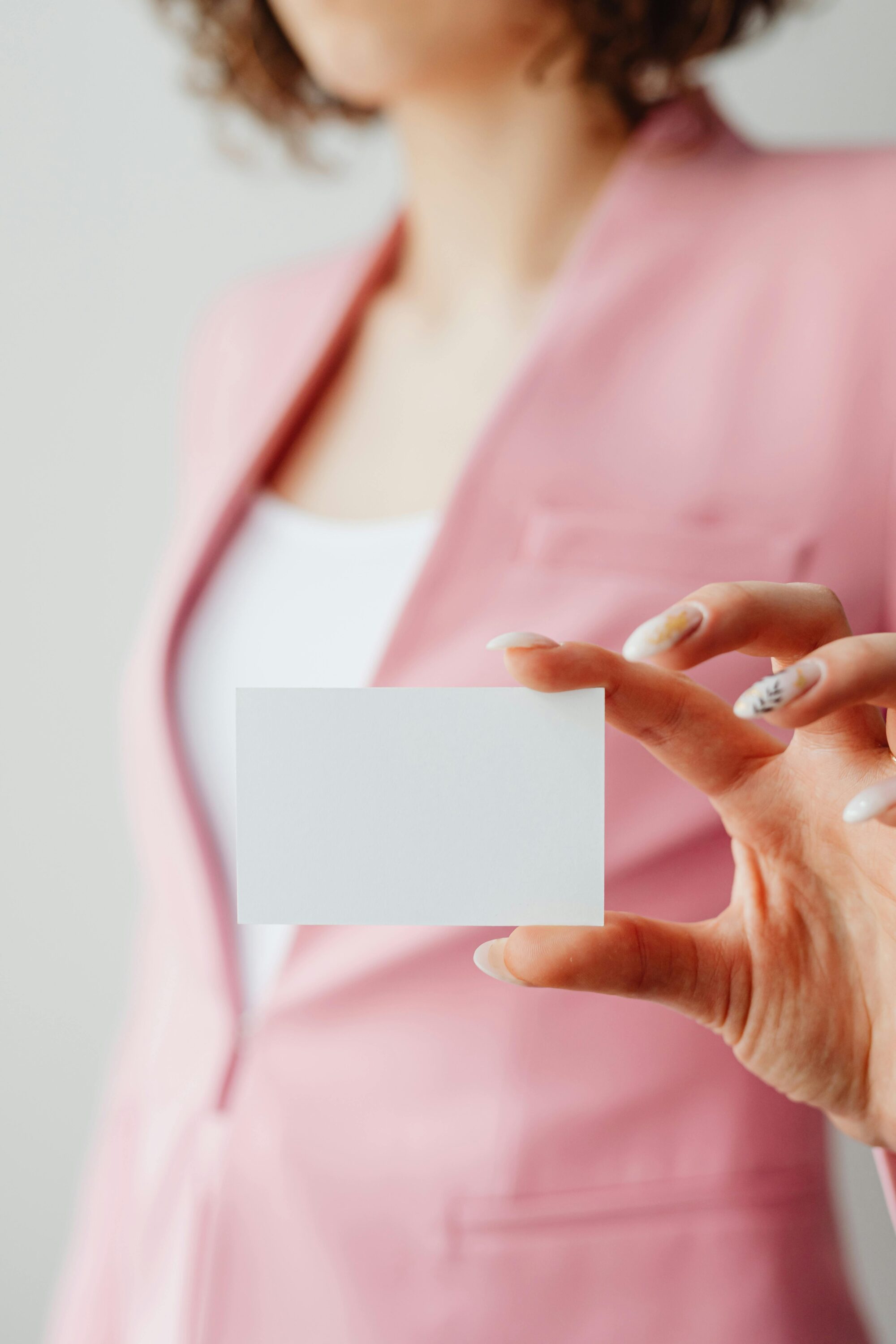 Woman in pink suit holding a blank business card — the perfect example of an image you might use when creating mockups.