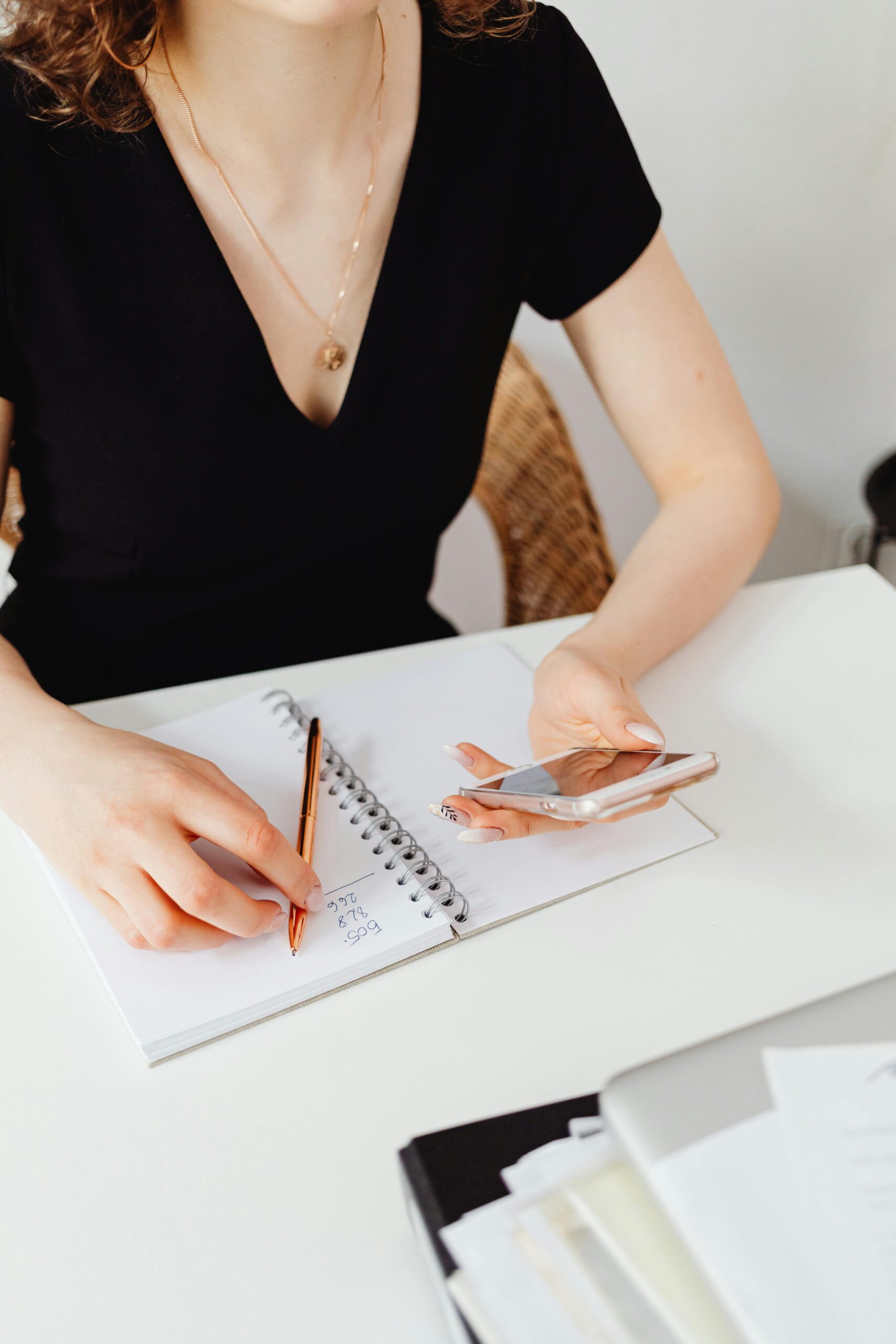 A woman sitting at a desk writing on a notebook as she plans out her tripwire funnel.