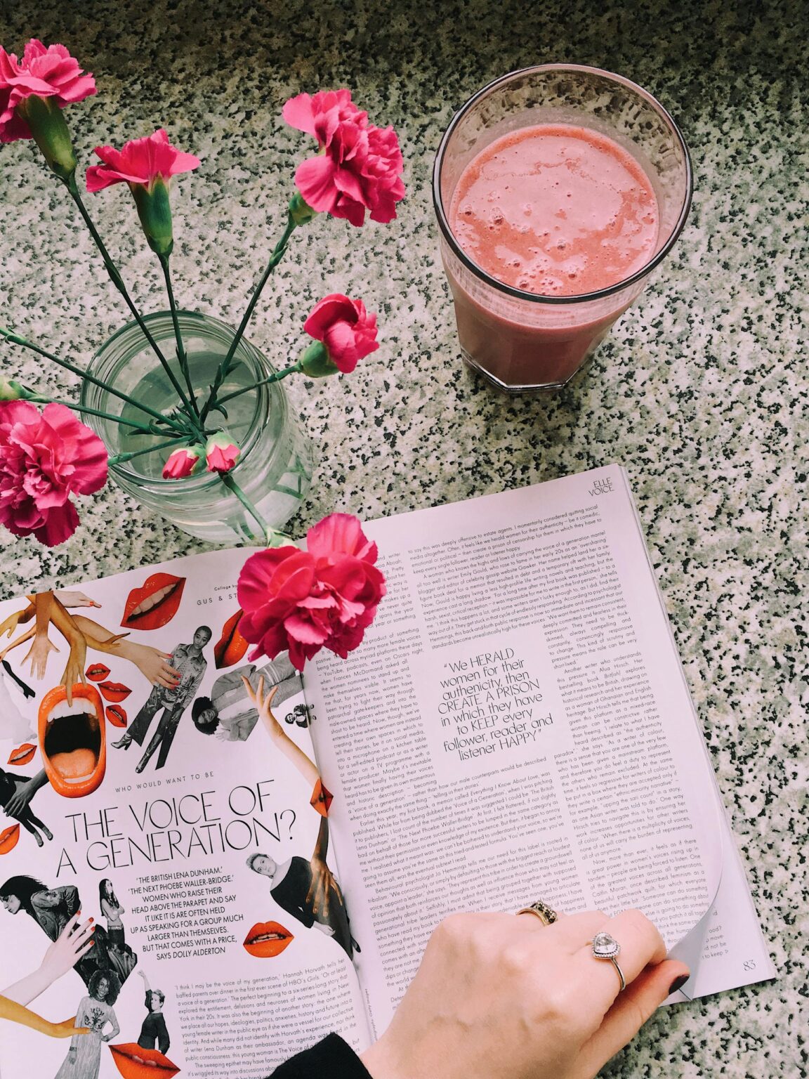 A top-down view of a magazine on a wooden table, surrounded by delicate flowers in soft tones and a vibrant pink smoothie in a glass, creating a fresh and inviting scene for implementing a DIY PR strategy.