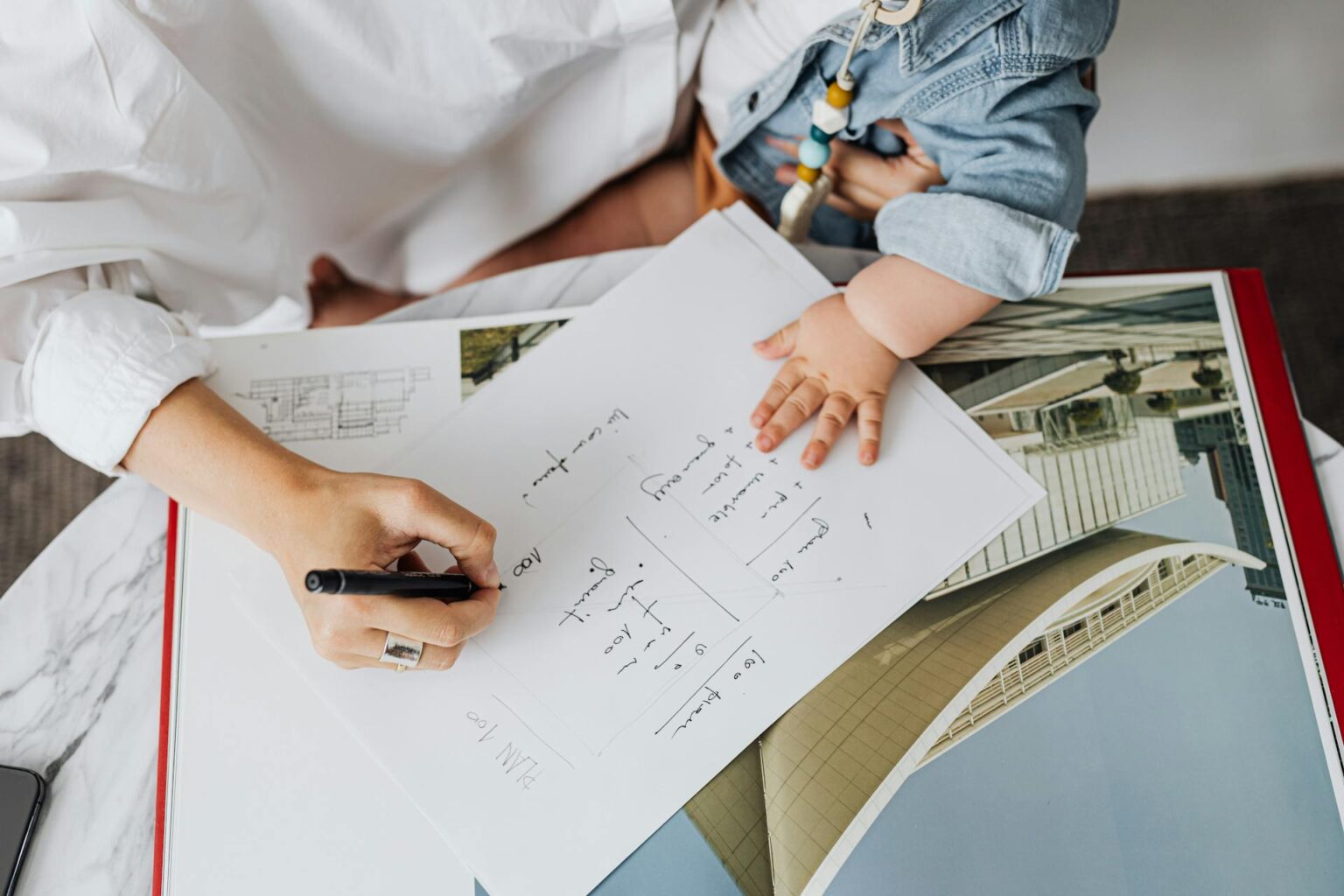 Woman holding her child as she writes down her notable highlights, looks through imagery, and decides what should go into her digital media kit.