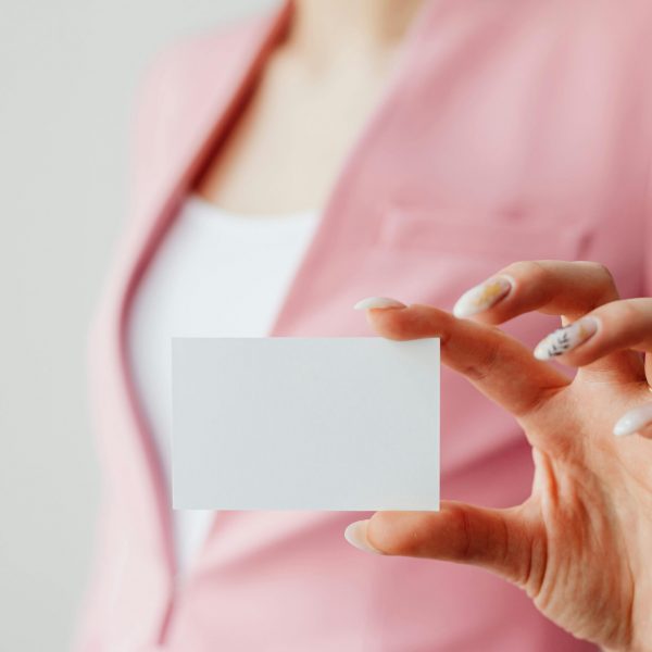 Woman in pink suit holding a blank business card — the perfect example of an image you might use when creating mockups.