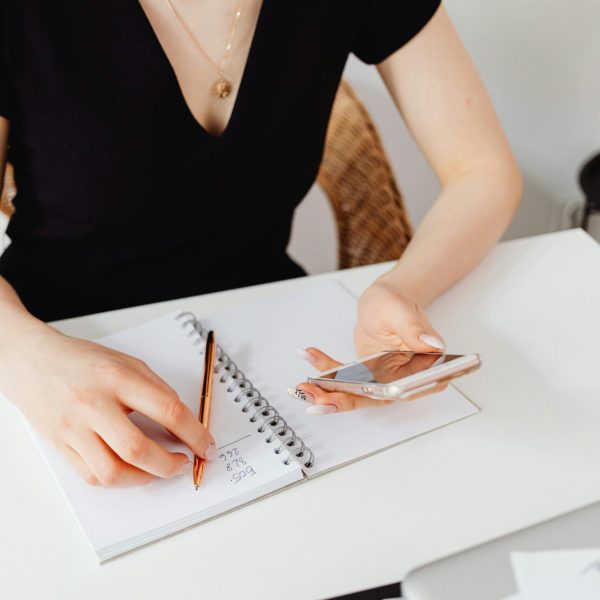 A woman sitting at a desk writing on a notebook as she plans out her tripwire funnel.